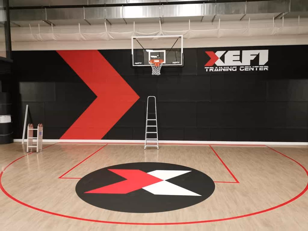 Vinilo de círculo central en el parquet de una cancha de baloncesto, con la canasta al fondo